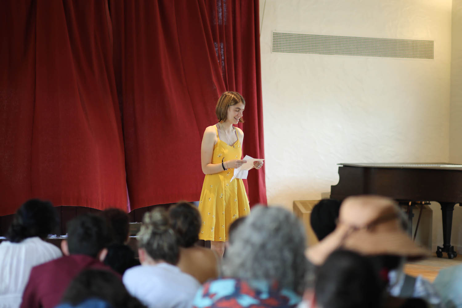 Girl in yellow dress reading aloud from a notebook on stage